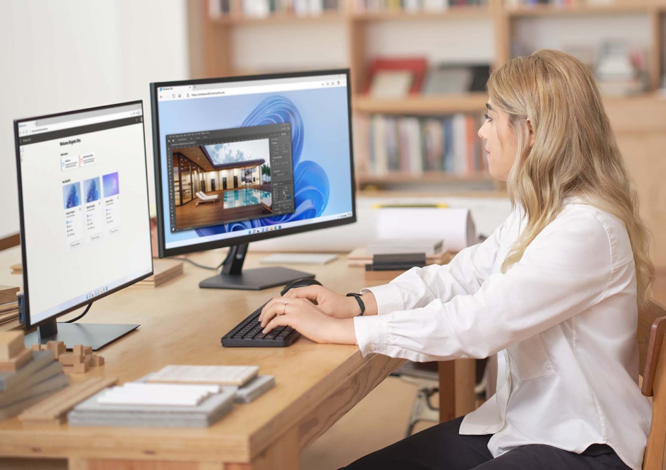 a woman sits at a desk in front of two monitors