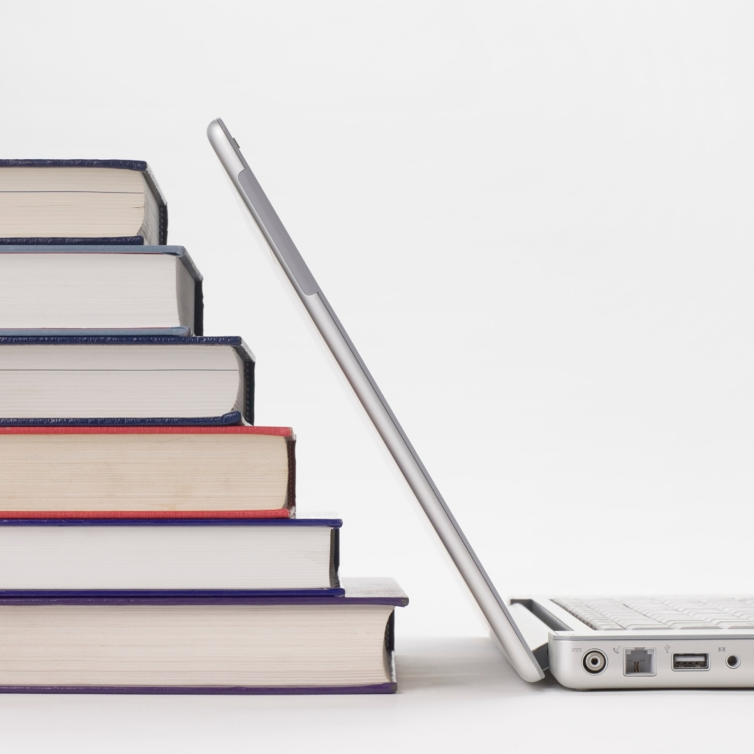 A laptop open with a stack of books behind the screen.