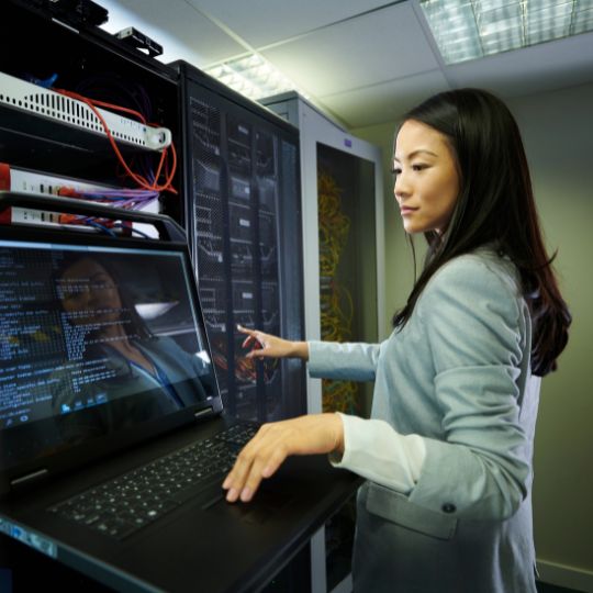 A person standing in front of a computer neat a server bank